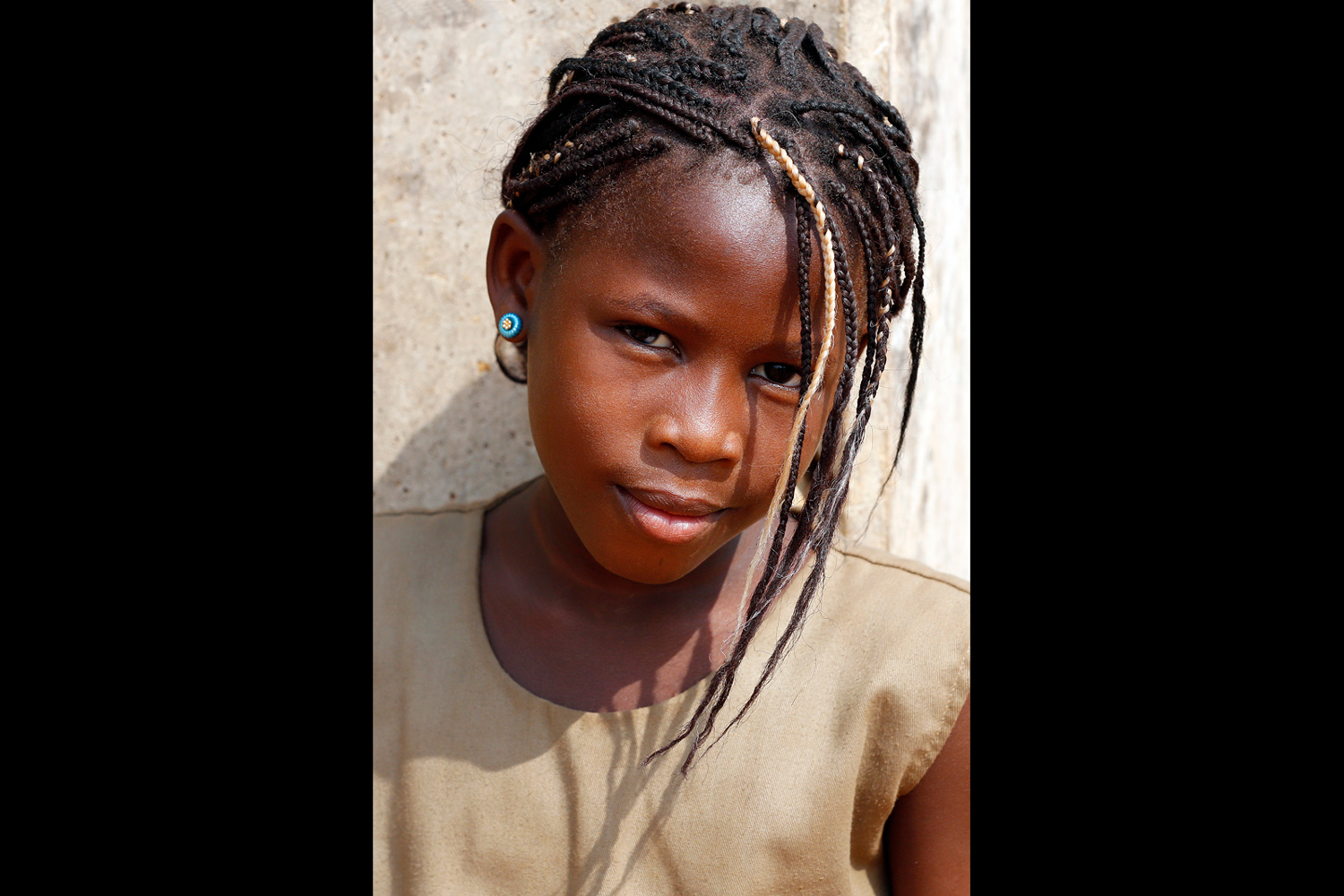 Portrait d’une écolière avec de fines nattes et un regard complice au Bénin en 2013