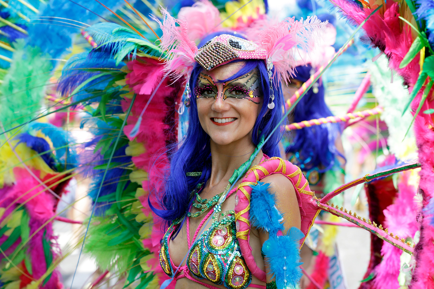Portrait rapproché d'une danseuse souriante coiffée de plumes roses, bleues et vertes.