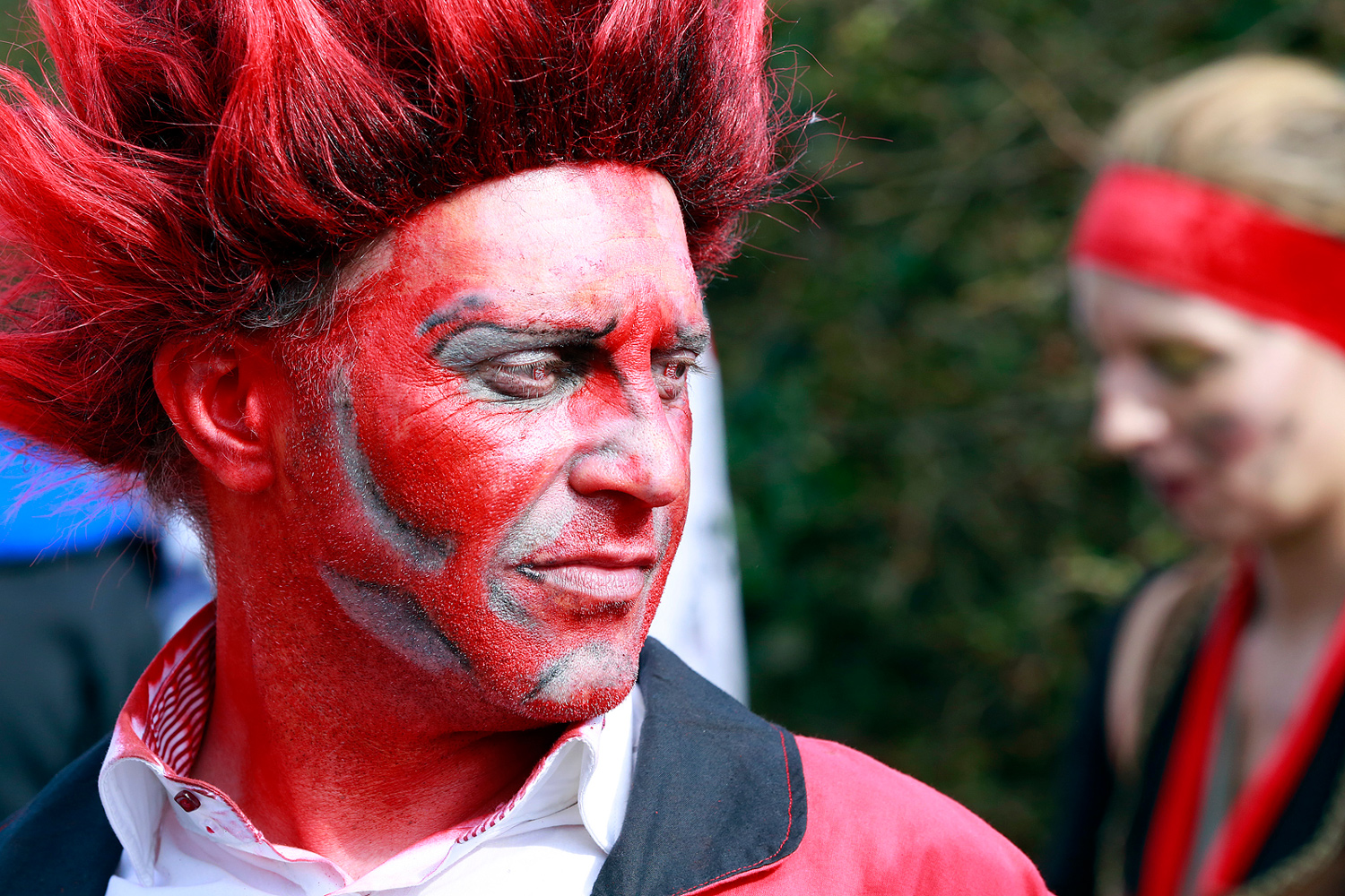 Portrait d'un carnavaleux maquillé entièrement en rouge avec une coiffure rouge dressée vers le haut, regardant vers la gauche.