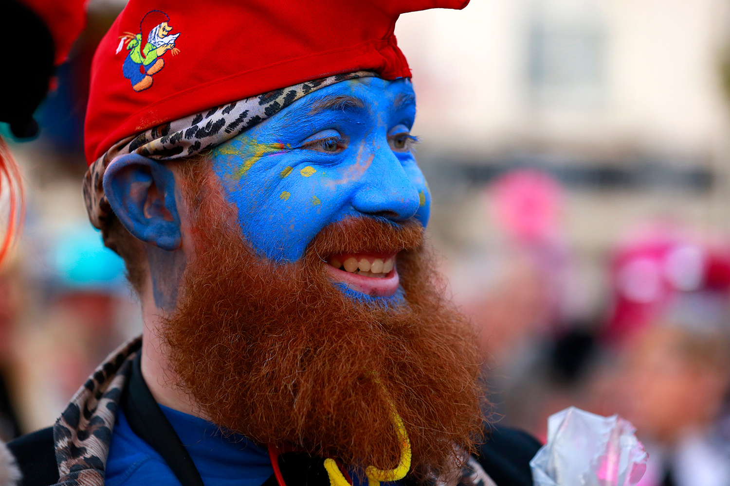 Portrait d'un carnavaleux barbu maquillé entièrement en bleu, coiffé d'un bonnet rouge et souriant pendant la Bande de Pitgam.