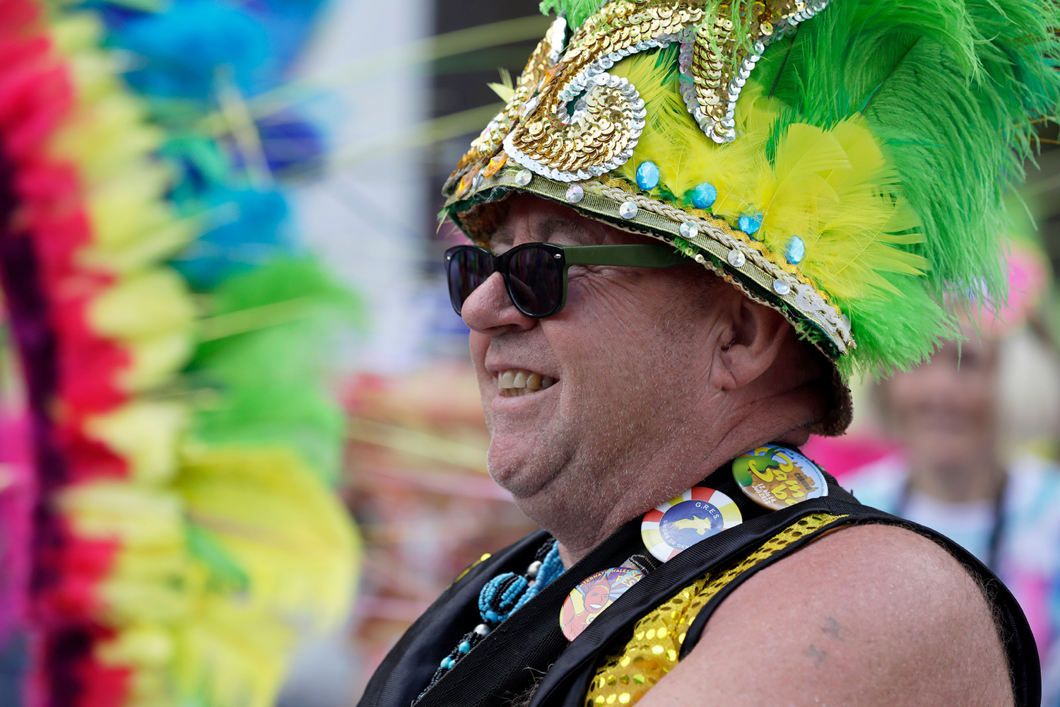 Portrait d'un participant souriant portant un chapeau vert et jaune décoré de plumes.
