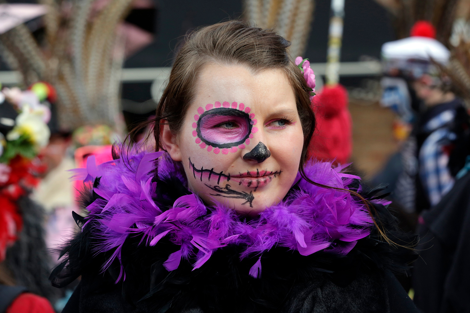 Portrait d'une jeune carnavalière portant un maquillage violet et noir inspiré d'une tête de mort mexicaine, accompagné d'un boa violet.