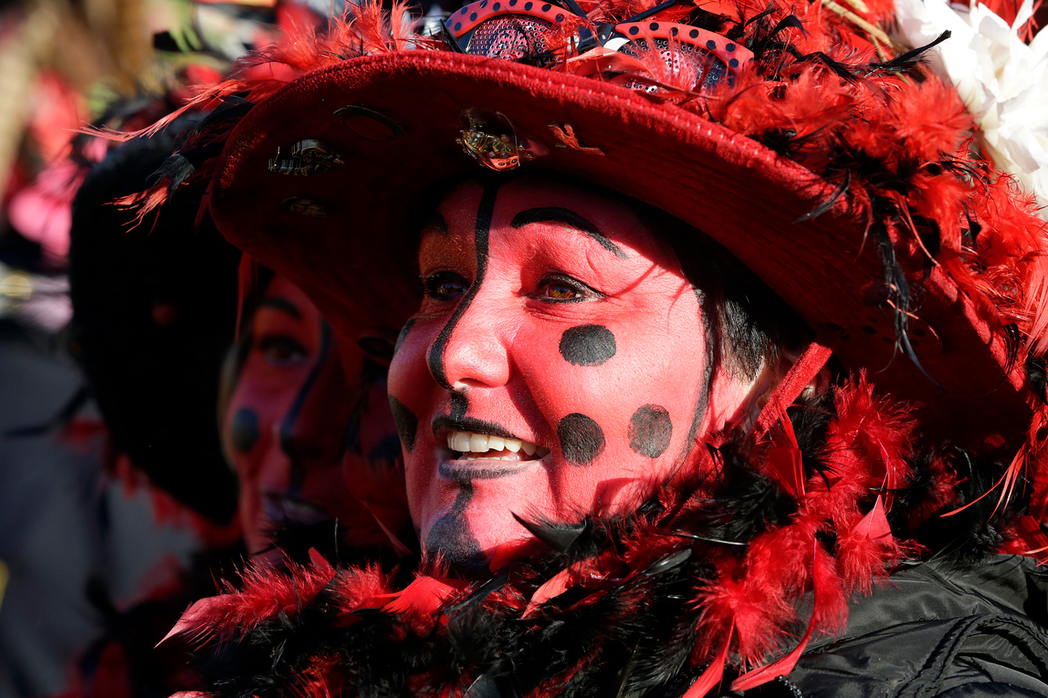 Portrait d'une carnavalière portant un chapeau rouge à plumes et un maquillage rouge orné de pois noirs.
