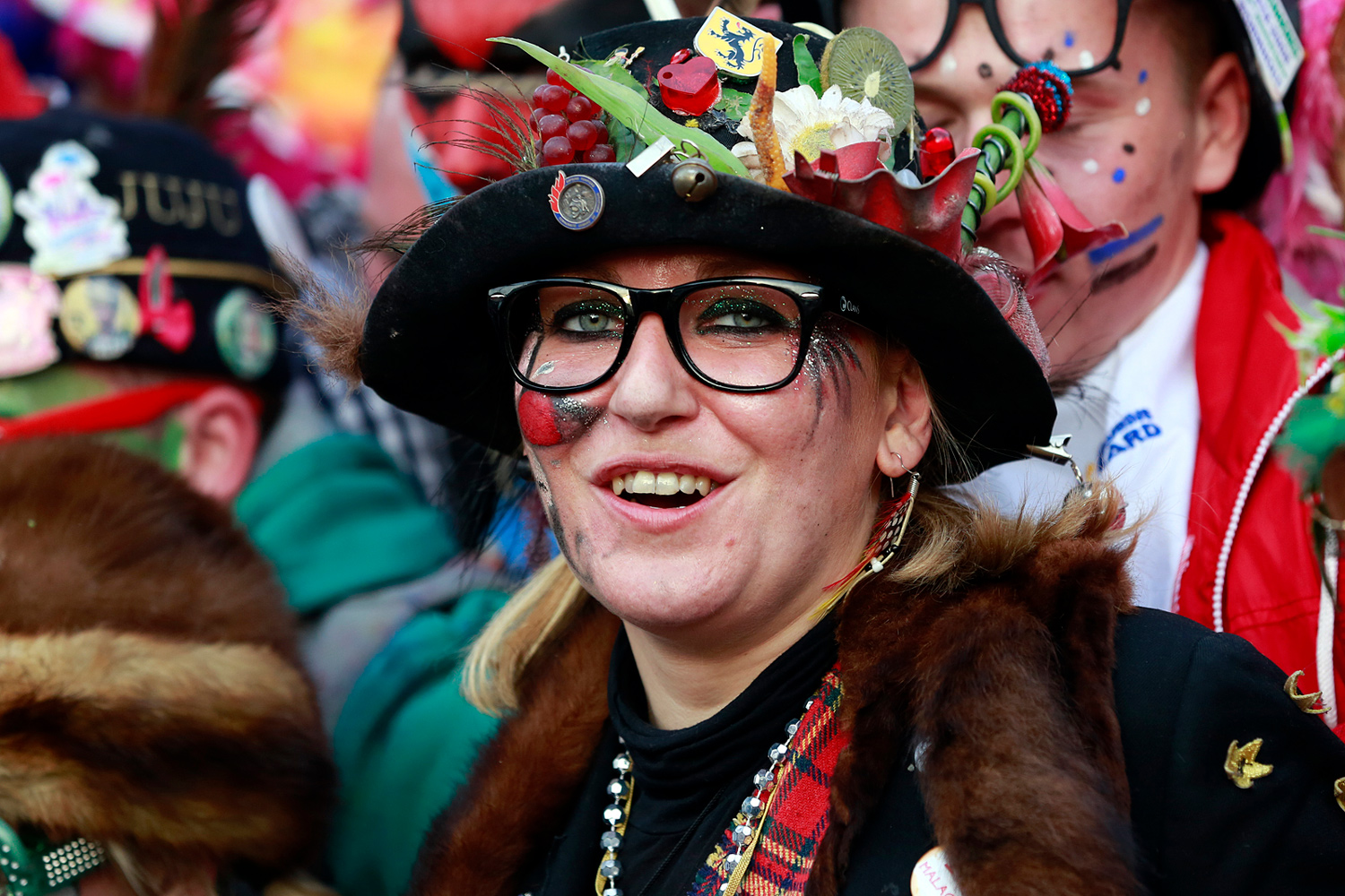 Portrait d'une carnavalière souriante portant un chapeau noir décoré de fleurs multicolores, de badges et d'accessoires, au cœur de la Bande de Pitgam.