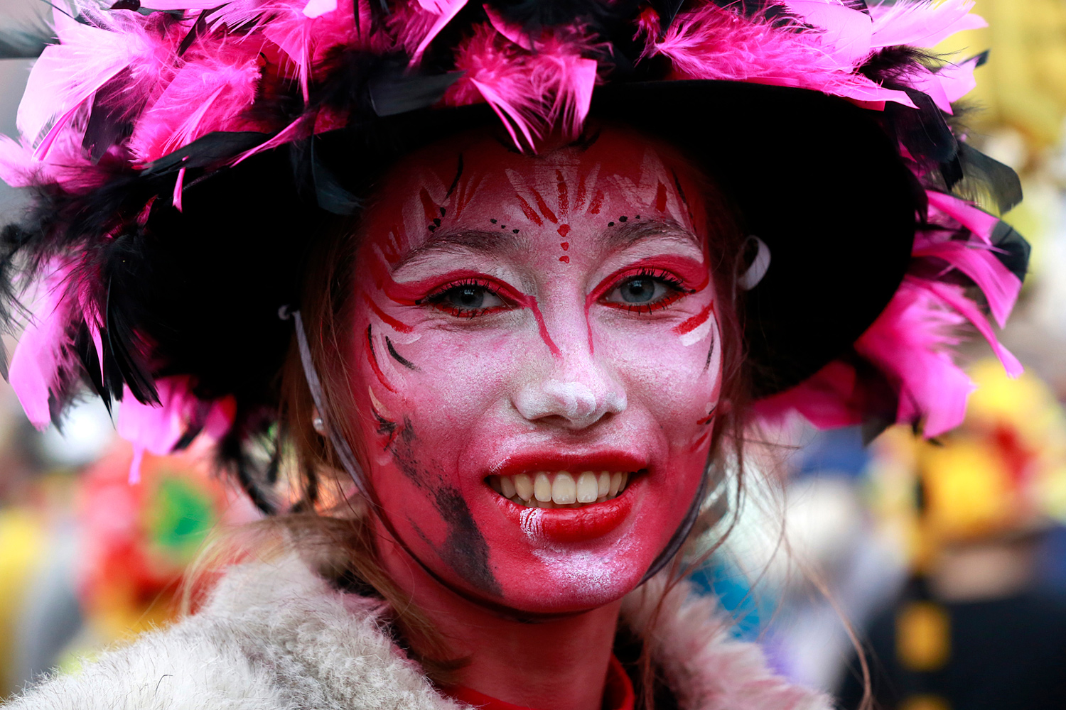 Portrait rapproché d'une carnavalière maquillée de rose et de blanc, coiffée d'un chapeau noir orné de plumes roses, lors de la Bande de Pitgam du Carnaval de Dunkerque.