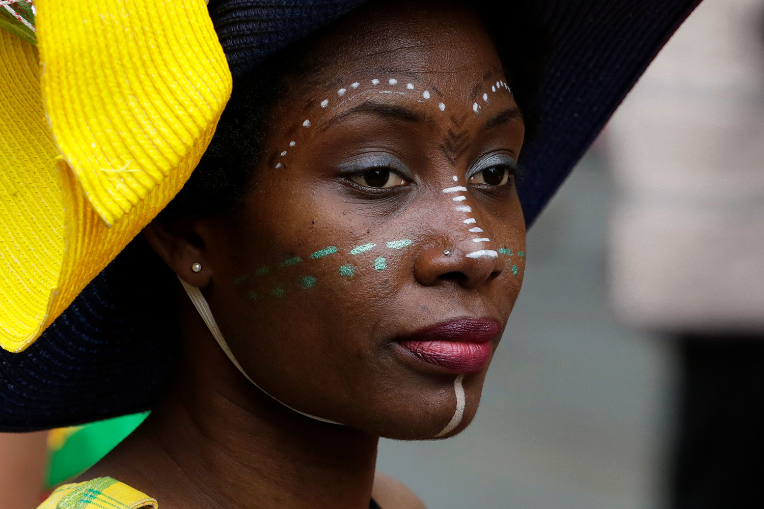 Portrait d'une participante portant un large chapeau noir et jaune et un maquillage traditionnel.