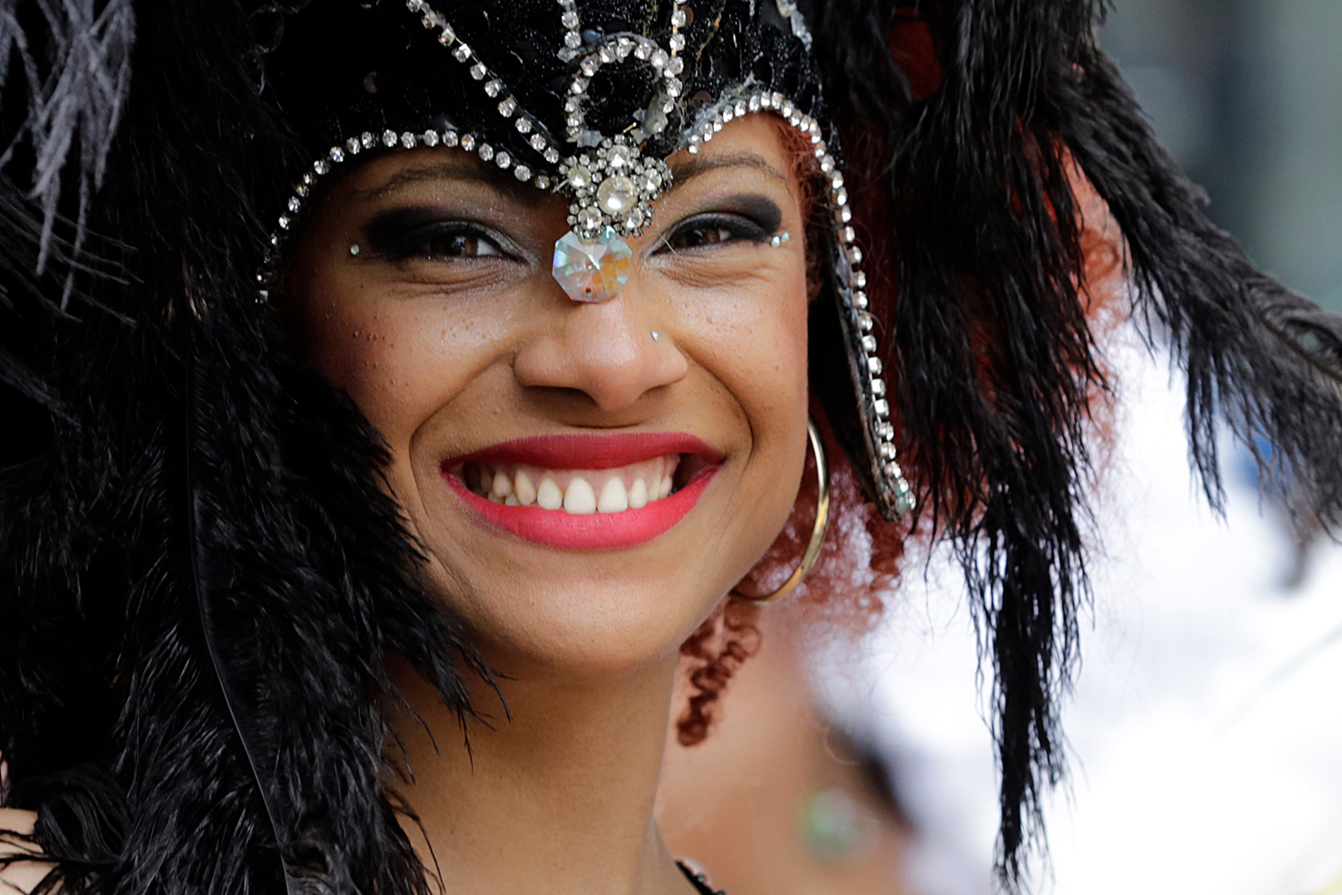 Portrait rapproché d'une danseuse souriante coiffée de plumes noires et d'un bijou frontal.