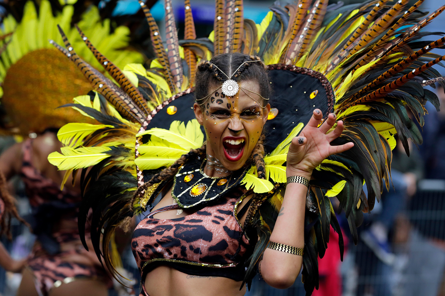 Danseuse portant une imposante coiffe de plumes jaunes et noires, souriante, lors du Carnaval Tropical de Paris.