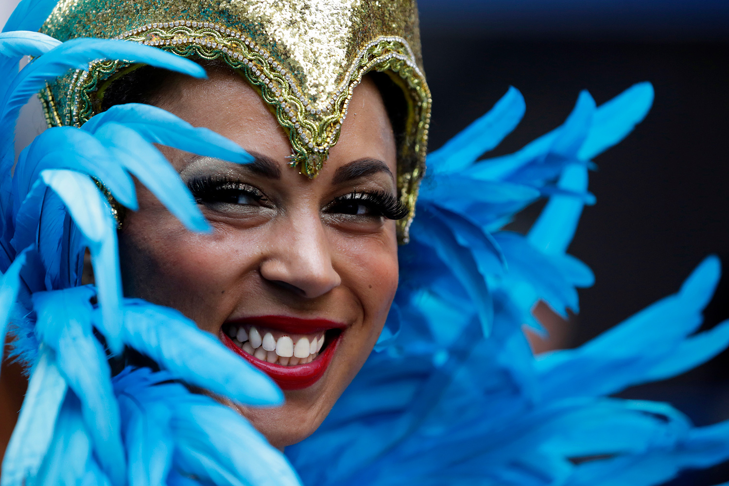Portrait d'une danseuse souriante entourée de grandes plumes bleues.