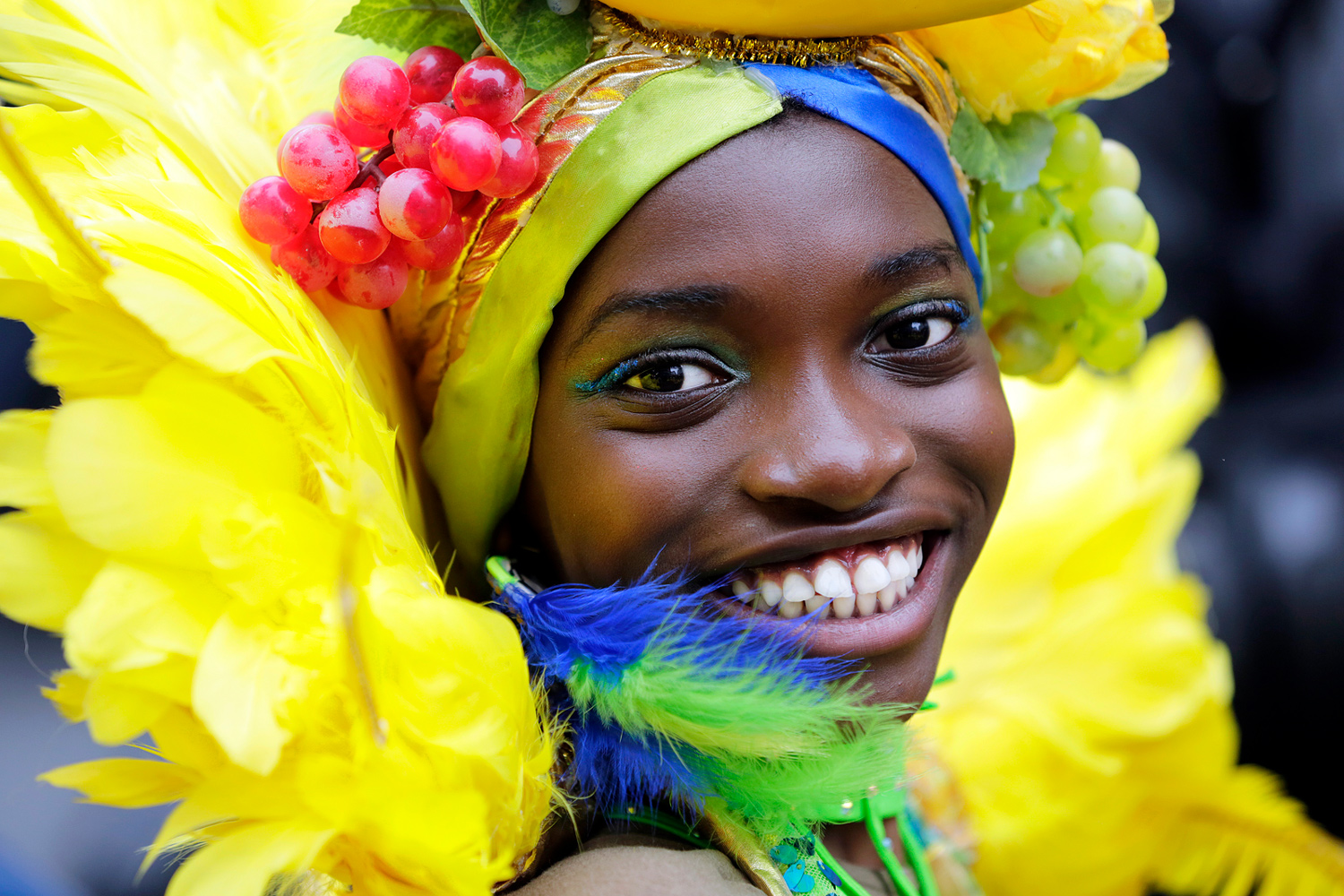 Jeune danseuse souriante entourée de plumes jaunes, bleues et vertes.