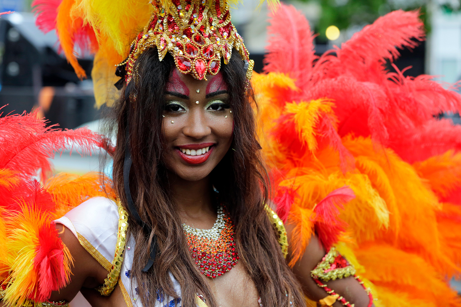 Danseuse portant une coiffe rouge et or ainsi qu'un costume composé de plumes orange.