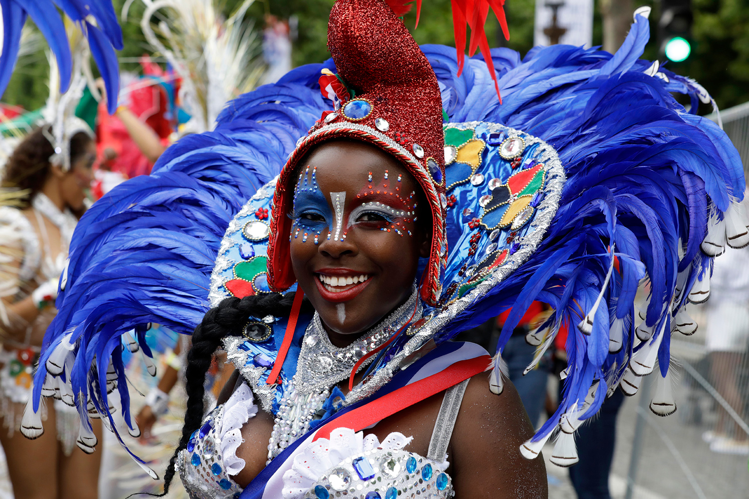 Portrait d'une danseuse souriante portant une imposante coiffe bleue décorée de plumes.