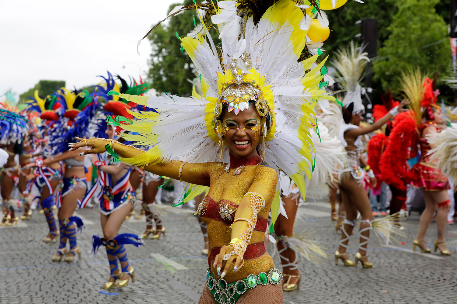 Danseuse souriante portant une grande coiffe blanche et jaune au milieu du cortège.