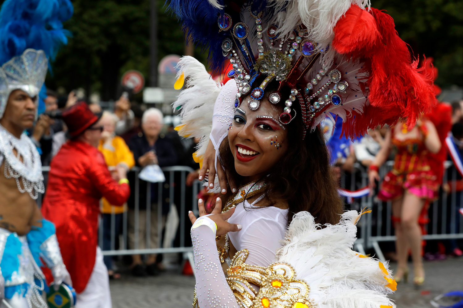 Danseuse se retournant vers le photographe dans un costume blanc agrémenté de plumes bleues et rouges.