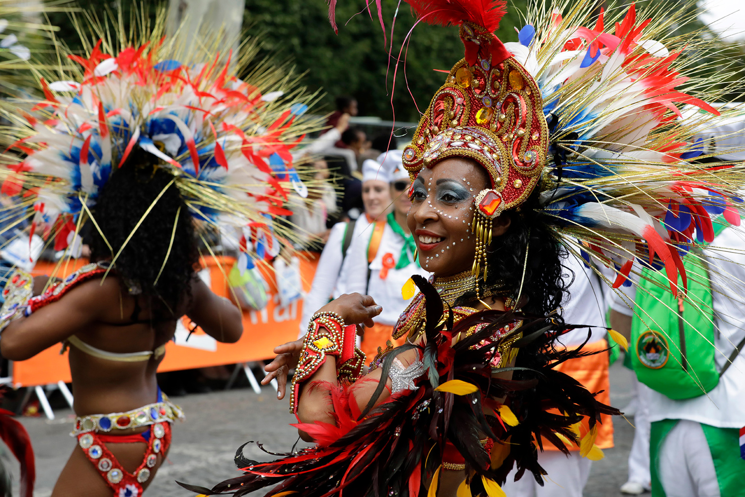 Portrait de profil d'une danseuse portant une coiffe rouge, noire et dorée décorée de plumes.
