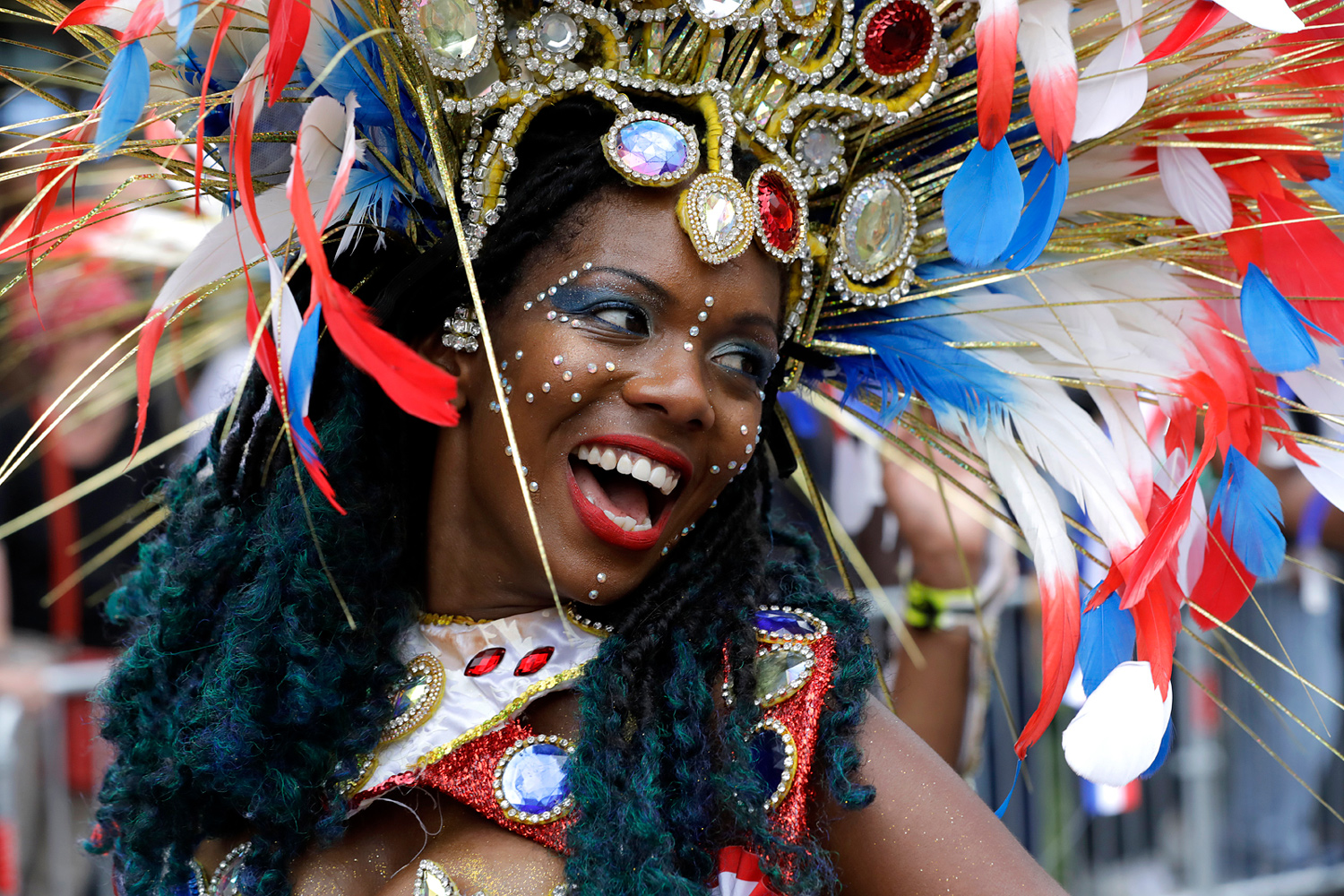 Portrait d'une danseuse éclatant de rire sous une grande coiffe blanche, bleue et rouge.