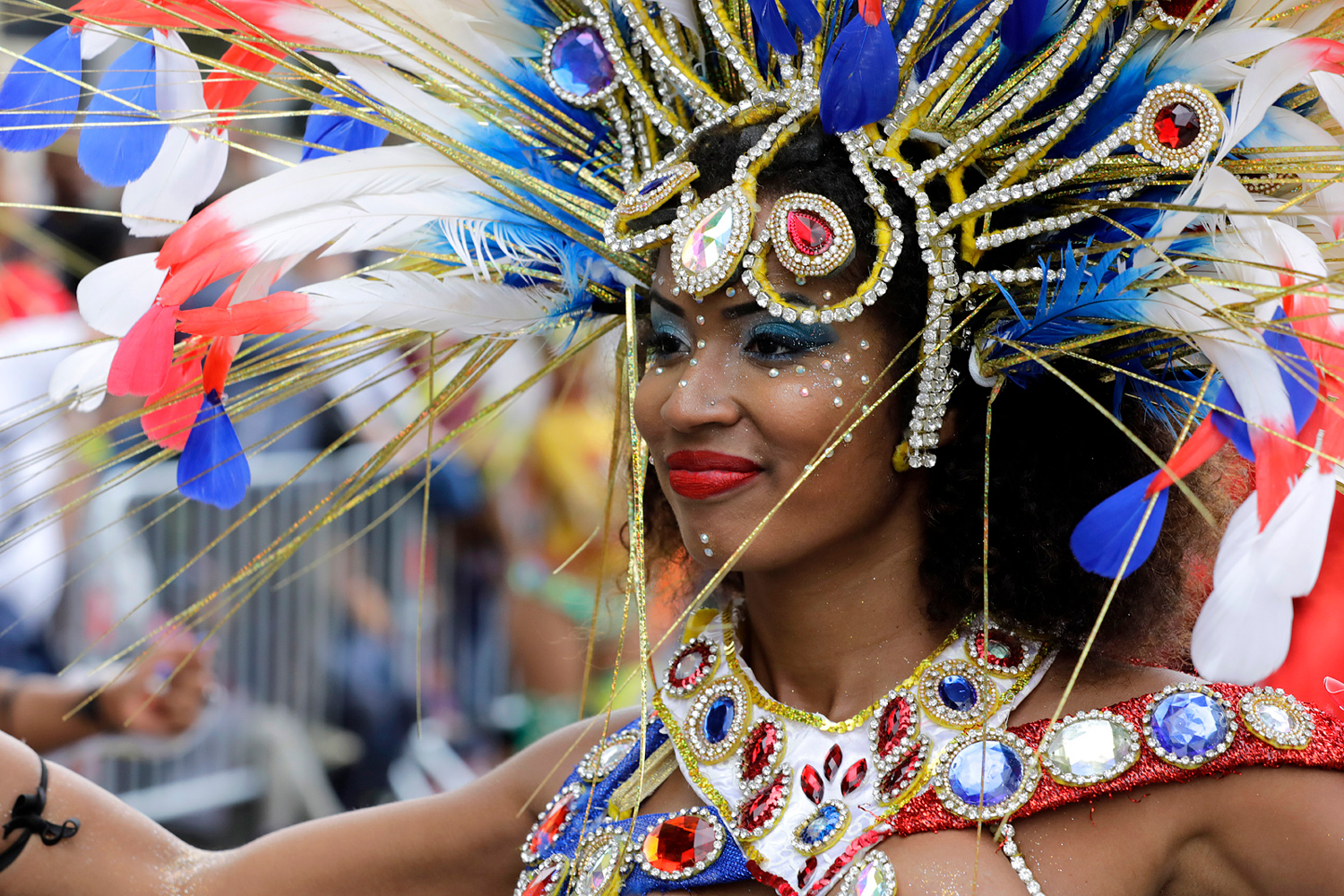 Portrait de profil d'une danseuse portant une coiffe blanche, bleue et rouge ornée de plumes.