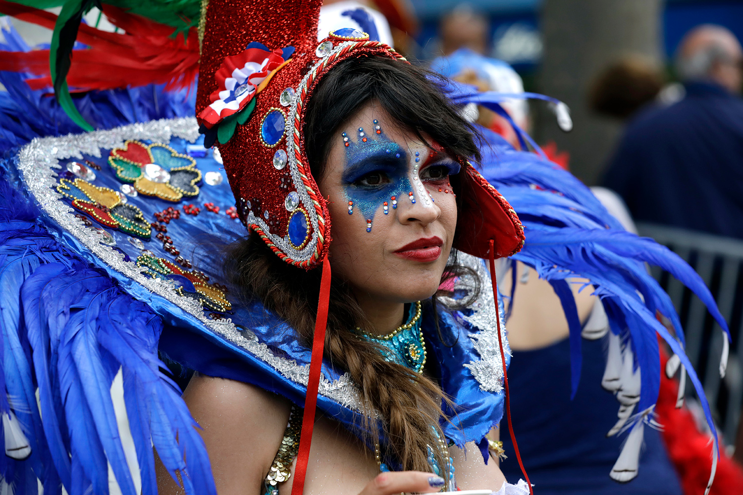 Portrait d'une danseuse portant une coiffe bleue ornée de plumes et un maquillage bleu pailleté.