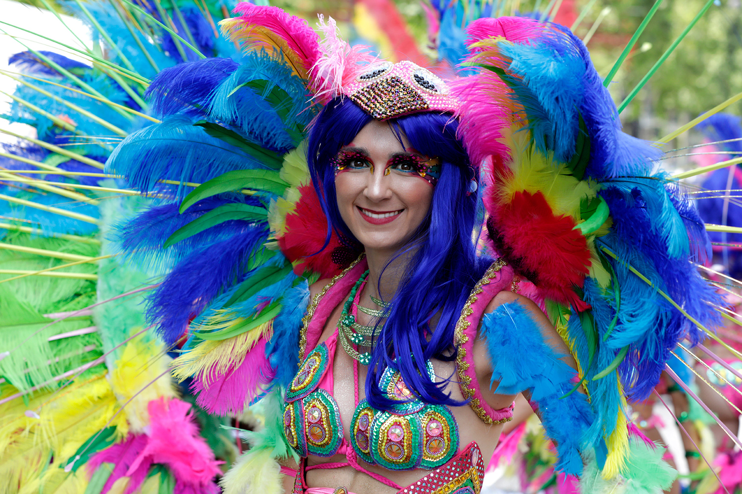 Portrait frontal d'une danseuse entourée de grandes plumes bleues, vertes et roses.