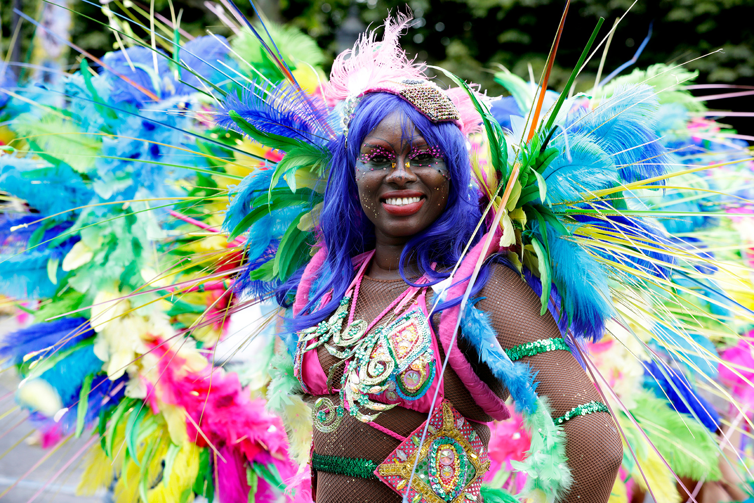 Portrait d'une danseuse souriante au centre d'un costume composé de plumes bleues, vertes et roses.