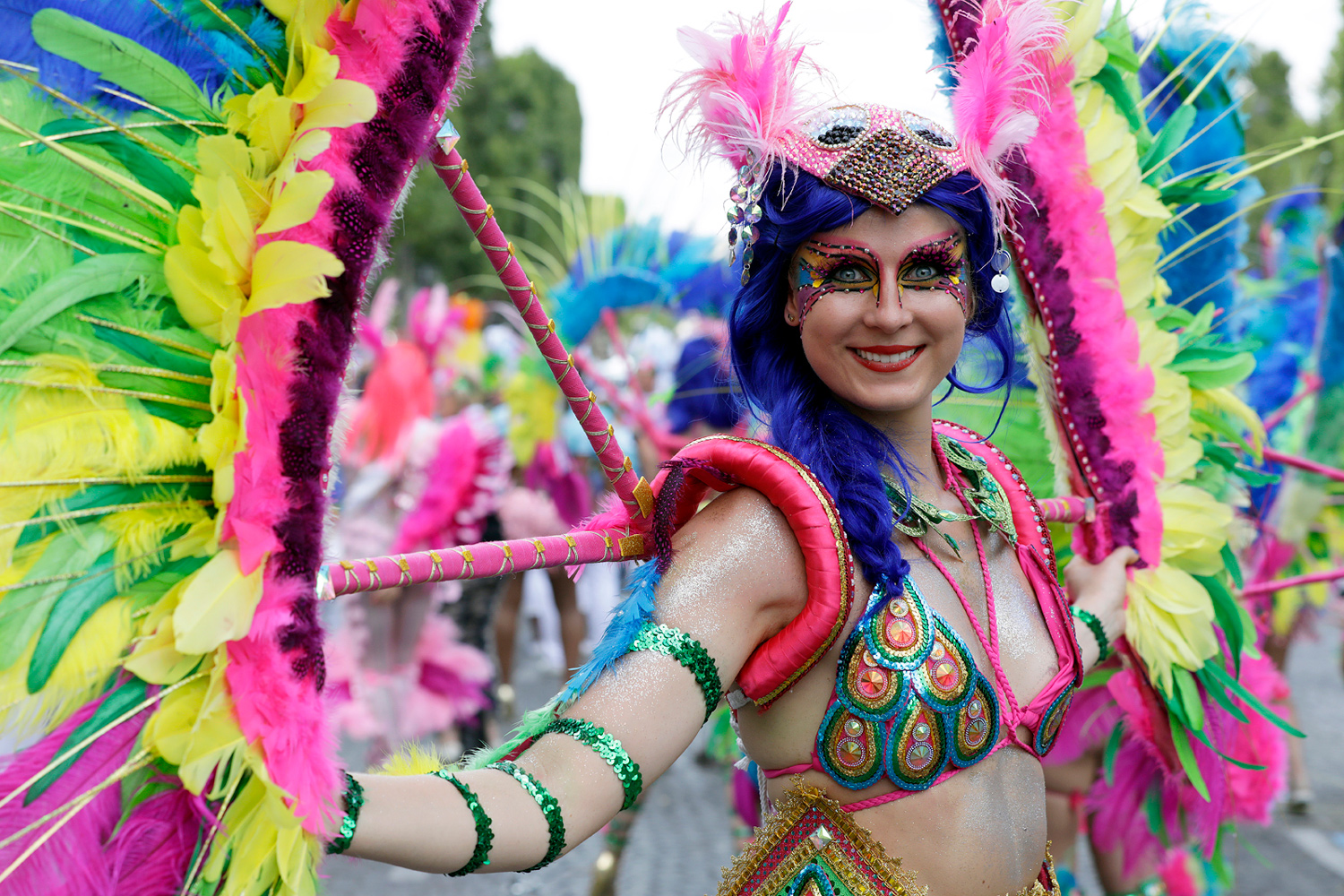 Portrait d'une danseuse souriante portant un costume rose, bleu et vert agrémenté de plumes colorées.