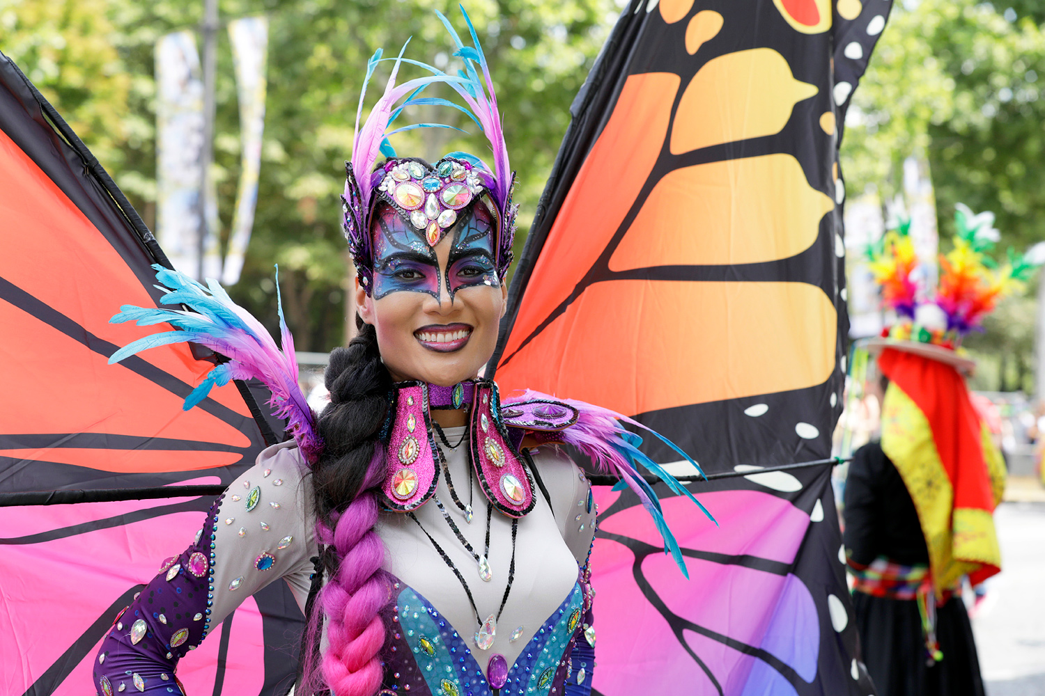 Portrait d'une danseuse déguisée en papillon avec de grandes ailes orange, violettes et noires.