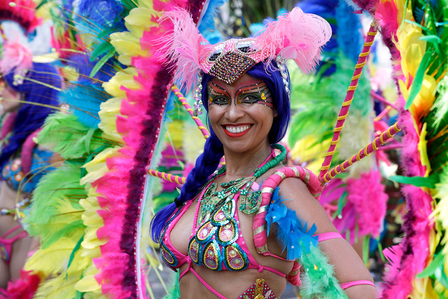 Portrait d'une danseuse souriante vêtue d'un costume multicolore composé de plumes roses, bleues et vertes.