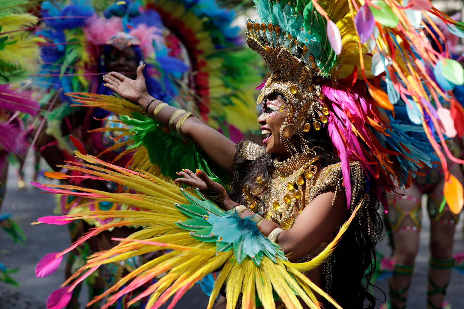 Portrait de profil d'une danseuse portant une spectaculaire coiffe multicolore composée de longues plumes.