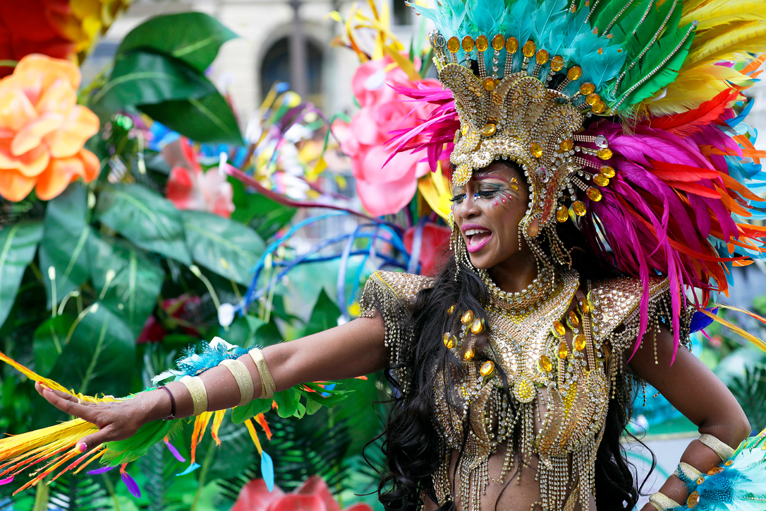 Danseuse exécutant une chorégraphie devant un char décoré de fleurs tropicales, vêtue d'un costume doré et multicolore.