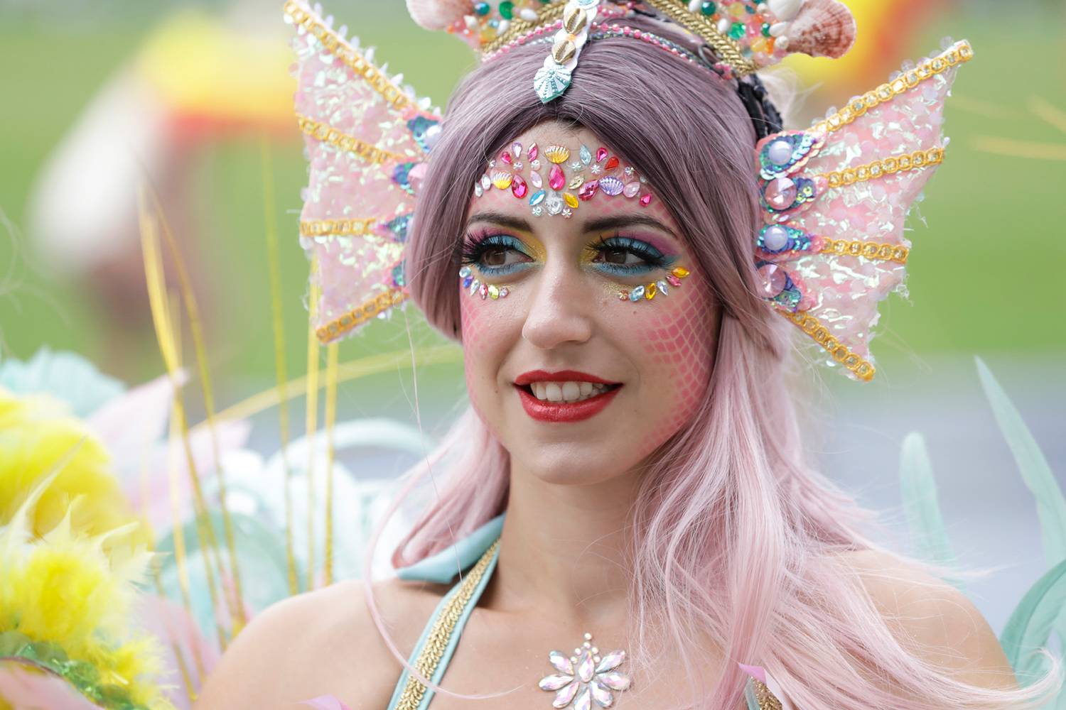 Portrait d'une danseuse aux cheveux roses portant une coiffe pastel et un collier en forme de fleur.