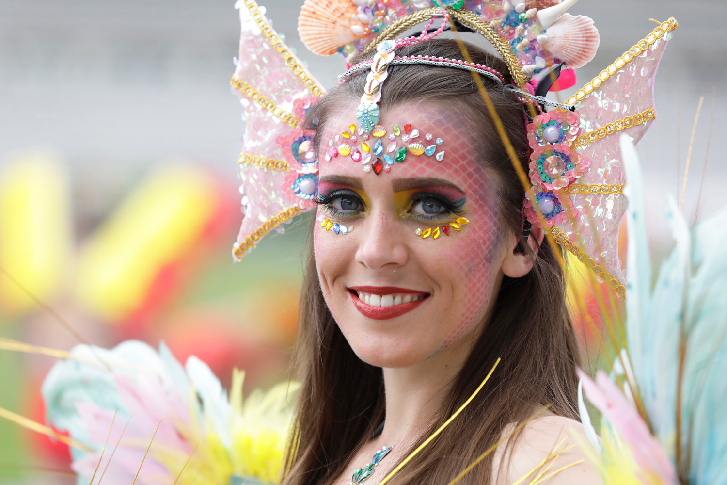 Portrait d'une danseuse souriante portant une coiffe rose et un maquillage orné de strass multicolores.
