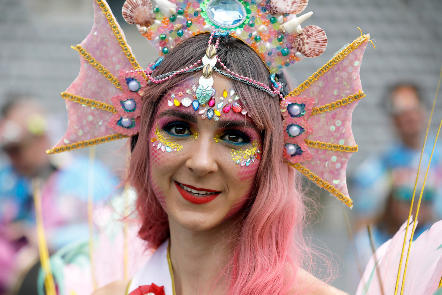 Portrait d'une danseuse portant une coiffe rose ornée de coquillages, de bijoux et d'un maquillage scintillant.