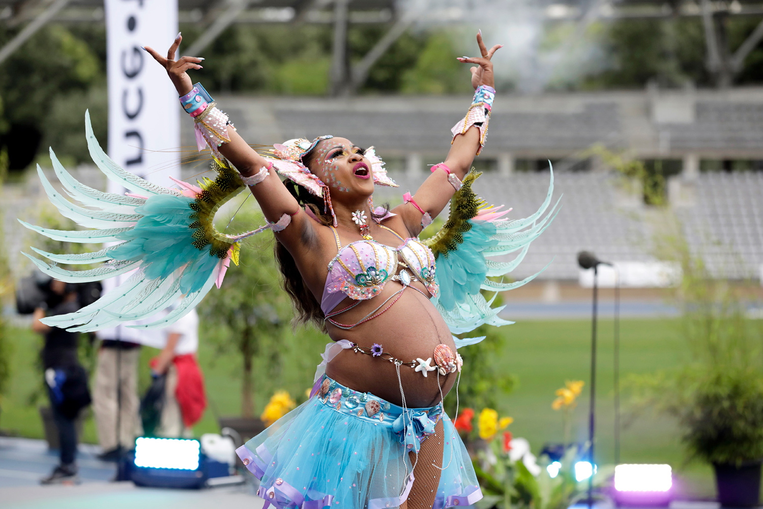 Danseuse levant les bras vers le ciel dans un costume pastel aux ailes déployées.