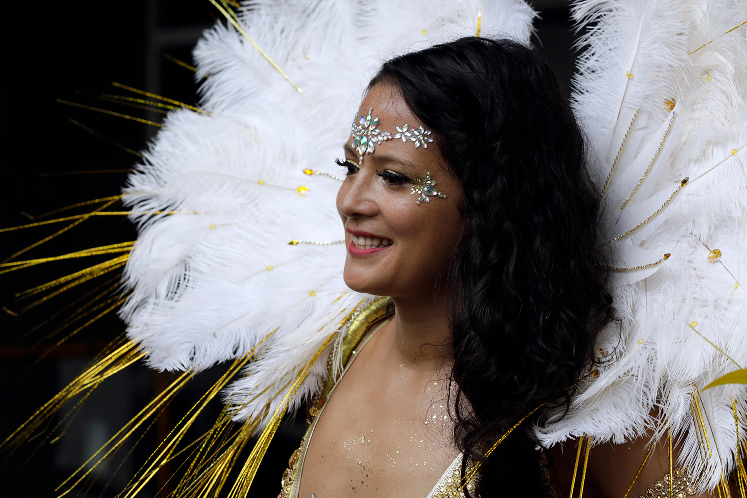 Portrait de profil d'une danseuse portant un costume blanc et or orné de grandes plumes.