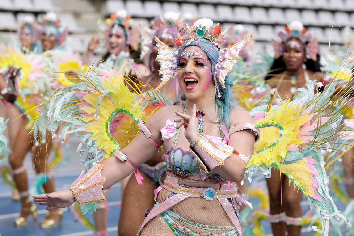 Danseuse souriante en costume pastel levant les bras pendant le défilé.