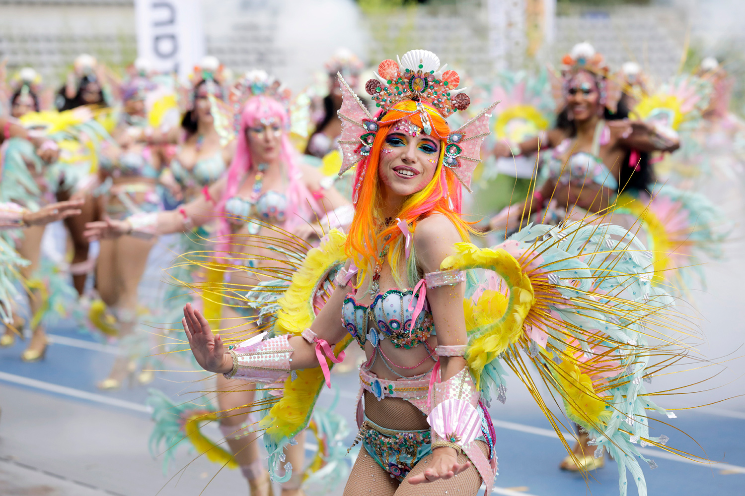 Danseuse aux cheveux orange évoluant devant son groupe dans un costume aux plumes jaunes et pastel.