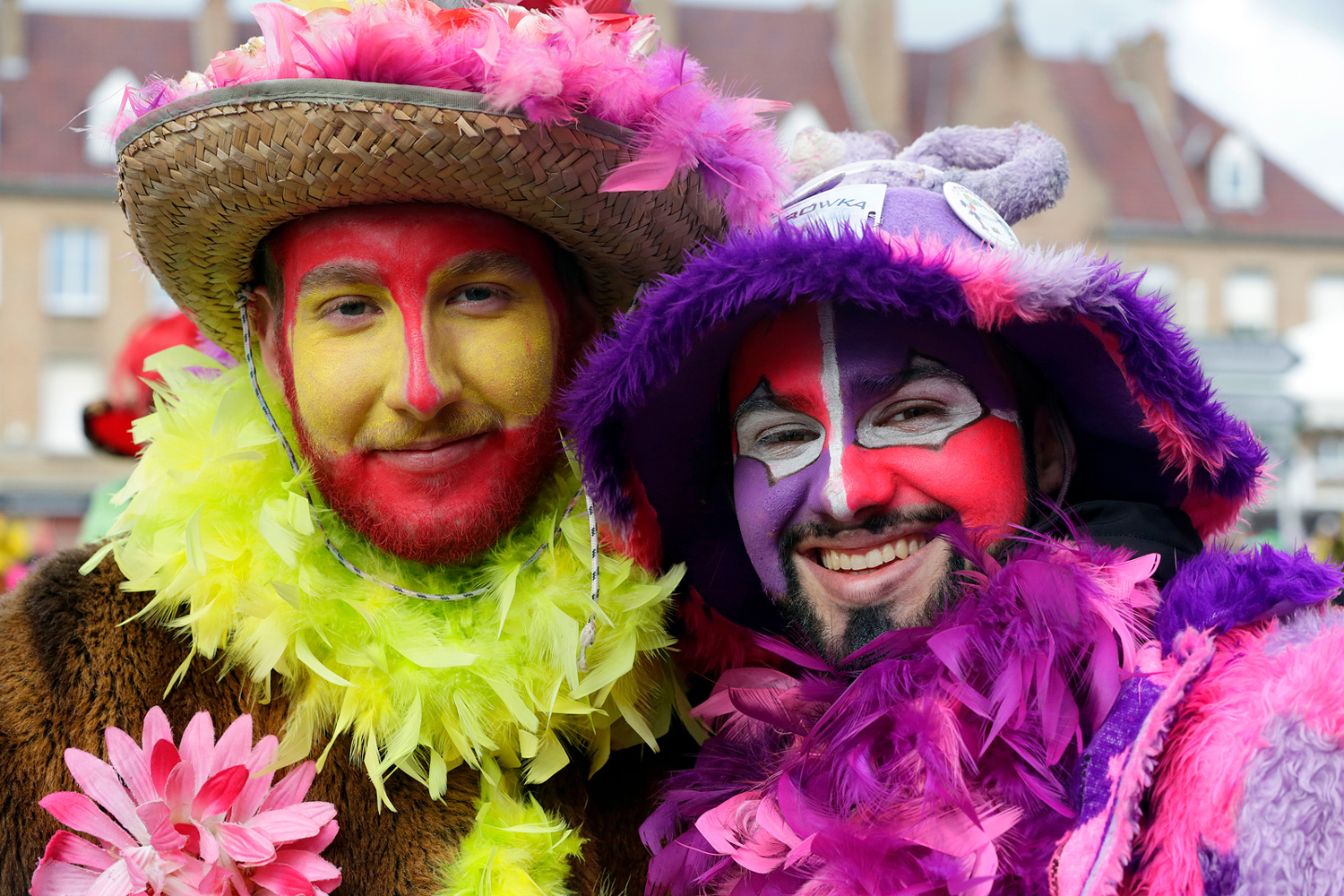 Deux carnavaleux costumés posent côte à côte, vêtus de boas colorés, de chapeaux décorés de plumes et de maquillages aux couleurs vives lors de la Bande de Bergues.